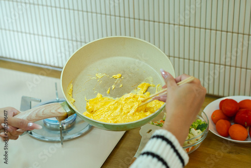 close up hand of woman in sweater stirs eggs, Cooking Scrambled Eggs in a green pan, capturing a warm homestyle cooking moment ideal for lifestyle and food content