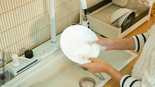 Фотография Close up of hands scrubbing a white plate with a foamy sponge at a clean modern