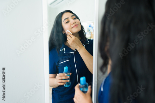 Latin woman applying facial toner to her skin with a cotton pad, following her daily skincare routine at home