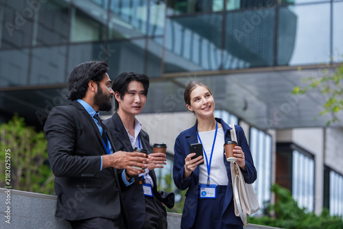 Fotografie Three young business professionals wearing conference badges relax against a low