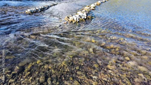Clear, clean mountain river is flowing in the shallows, low-head dams across the river, slow motion, natural background