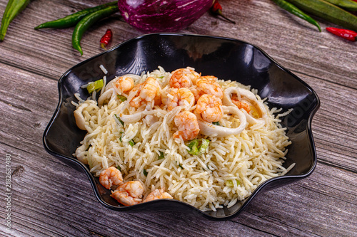 Foto Seafood basmati rice with prawns and squid rings in black bowl on rustic wooden