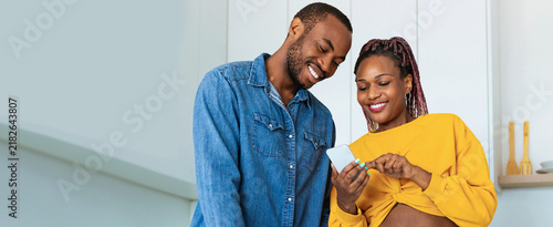 Foto Happy Black Couple Smiling Together While Looking At Smartphone In Cozy Kitchen, Enjoying Time Together, Engaged In Conversation