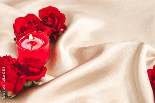 Fotografía Red roses and lit candle on smooth fabric with shine