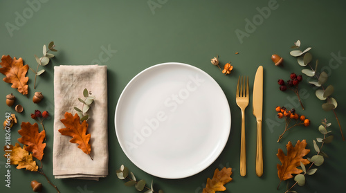 Elegant Thanksgiving dinner table setting mockup with empty white plate linen napkin gold cutlery oak leaves acorns and berries on dark green background top view