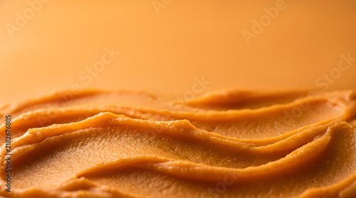 Close up of smooth pureed orange pumpkin spread in wavy strokes with soft lighting and wide empty space for text top view macro