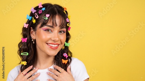 Young woman with colorful butterfly and star hair clips and bright makeup smiles against a yellow background