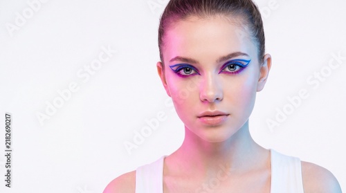 Woman with vibrant blue and pink graphic eyeliner and hair pulled back looking forward against a pastel background