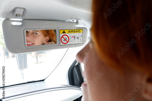 Redhead woman adjusting earring using car mirror