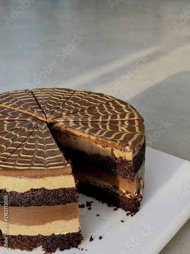 Quadro su tela Sliced layered chocolate caramel cake with spiderweb glaze icing in sunlight