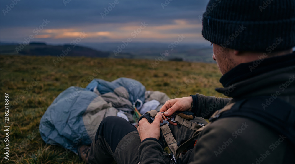 Fototapeta premium Paraglider preparing equipment on grassy hill at dusk