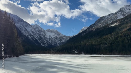 Scenic Panning Shot of Frozen Jägersee Lake in Kleinarl, Austrian Alps, during Winter Sunny Day, Surrounded by Snow-Covered Mountains and Pine Forest.
