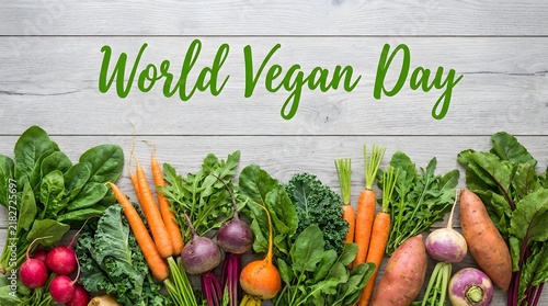 World vegan day text written on a rustic white wooden background with a border of fresh organic vegetables and greens