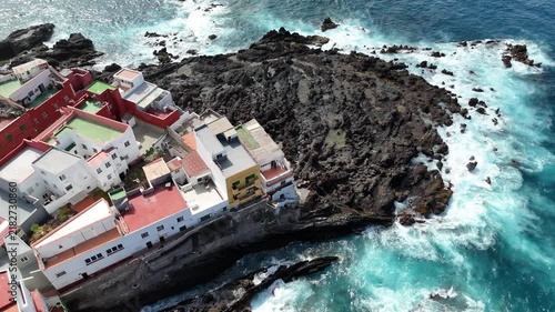 Top View of Puerto de la Cruz in Tenerife, showing a Picturesque Coastal Bay with Colorful Houses and Dramatic Rocky Coastline as Waves Crashing against the Shore of the Atlantic Ocean.