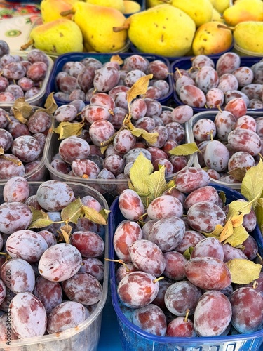 Fresh ripe plums for sale at farmers market, juicy purple fruit displayed on wooden counter