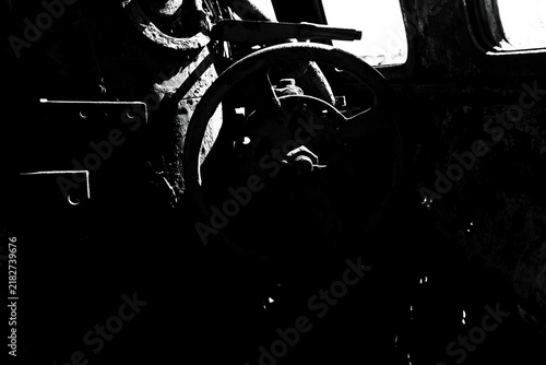 Black and white abstract close up of a rusty steering wheel inside an abandoned vintage train cabin