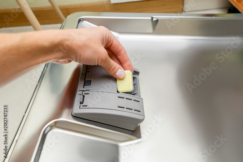 Woman hand putting multifunction tablet,detergent into dishwasher.Household chores,duties with modern kitchen appliance.Everyday home routine