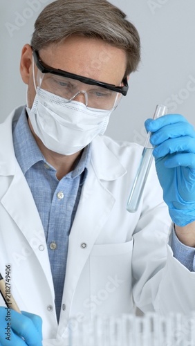 Scientist performing a scientific experiment in a laboratory. Holding a test tube with a liquid. Wearing a lab coat. Blue protective gloves. A face mask