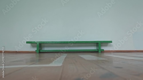 Single miniature green wooden bench standing alone in an empty room. Minimalist scene with a wooden floor and a plain white wall background