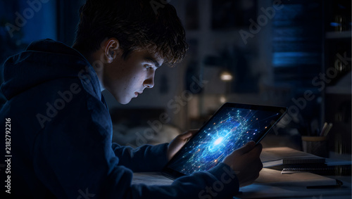 Focused High School Student in Dark Room Illuminated by Advanced AI Tablet