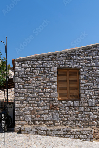 Traditional stone house facade with wooden window shutters and clear sky