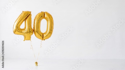 Gold number 40 foil balloons floating on a clean white background with copy space, festive decoration for 40th birthday, anniversary, milestone and celebration concepts.