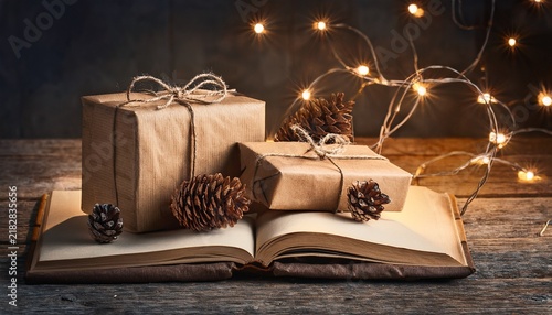wrapped gifts with string light on book and pinecones on rustic wooden table