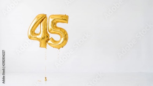 Gold number 45 foil balloons floating on a clean white background with copy space, festive decoration for 45th birthday, anniversary, milestone and celebration concepts.