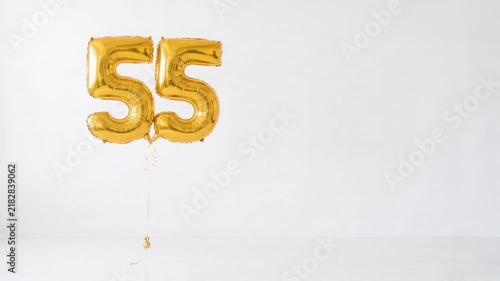 Gold number 55 foil balloons floating on a clean white background with copy space, festive decoration for 55th birthday, anniversary, milestone and celebration concepts.