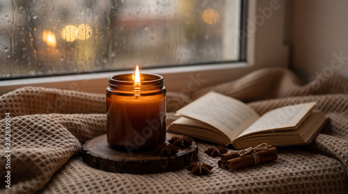 Принти на полотні Aromatic candle burning beside an open book on a cozy window sill with rainy day