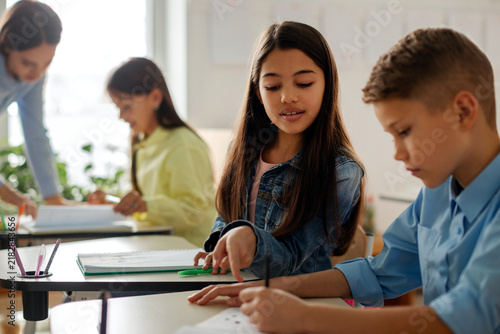 Obraz na plátne Elementary school girl explaining something to male classmate at desk