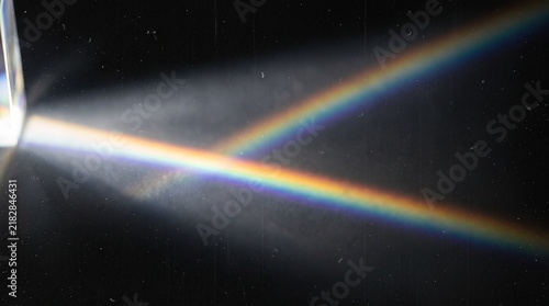 Light refraction through a glass prism splitting a light beam into a colorful rainbow spectrum in a dark room