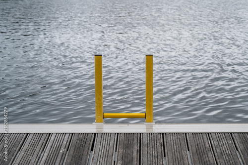 Foto Yellow marina ladder on wooden dock leading into rippling water with simple symm
