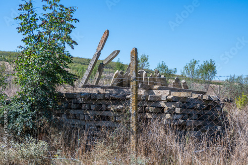 Foto a weathered stack of old concrete fence posts sitting haphazardly in tall, dry grass behind a wire fence on a rural hillside under a clear blue sky