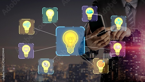 Fotografie Businessman holding smartphone with illuminated light bulb icons representing innovative ideas and concepts in modern urban landscape at night