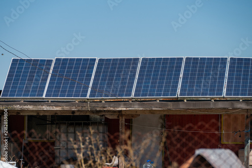 Canvastavla a row of modern blue solar panels installed on the weathered wooden roof of a rustic rural shed beneath a clear blue sky