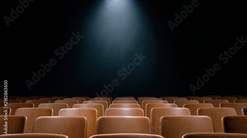 Empty wooden theater seats illuminated by a single spotlight against a dark background.