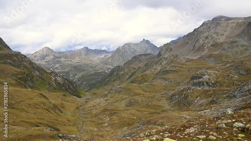 Rugged alpine valley with rocky slopes, grassland and cloud-covered mountain peaks in the Swiss Alps.