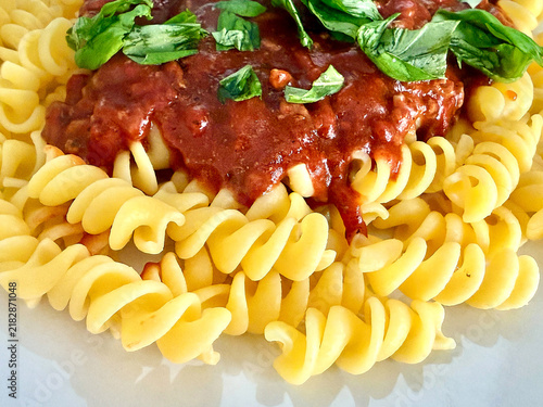 Close up view of fuselli pasta with a rich tomato sauce and fresh basil leaves on a white plate