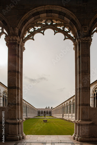 Historic Gothic cloister with elegant stone arches, carved columns, and a peaceful green courtyard illuminated by soft natural light