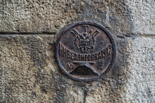 Foto A close-up of a rusty round metal geodetic marker (Nivelivka) from 1912, Russian Empire, embedded in an old brick wall