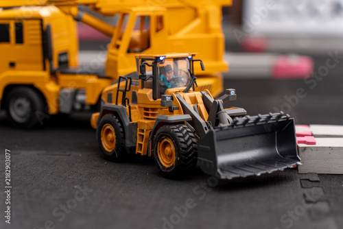 Detailed yellow scale model wheel loader with driver figurine inside cabin positioned on a miniature road set.