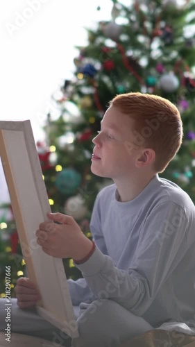 The teenager is holding a canvas in his hands and intently studying the painting. Its the eve of the New Year and Christmas.