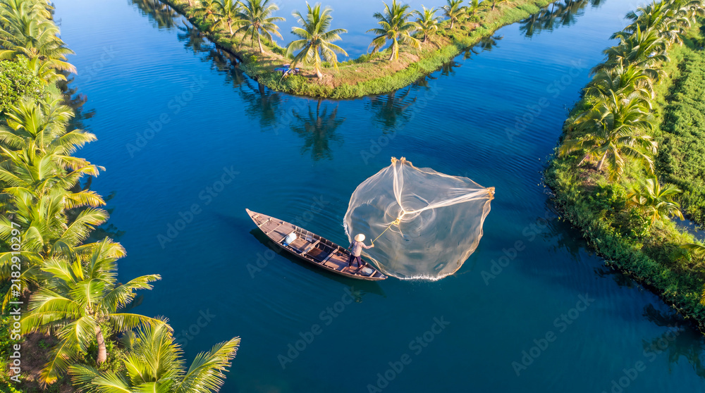 Obraz premium Fisherman casting a circular net from a traditional wooden boat in a tropical river canal