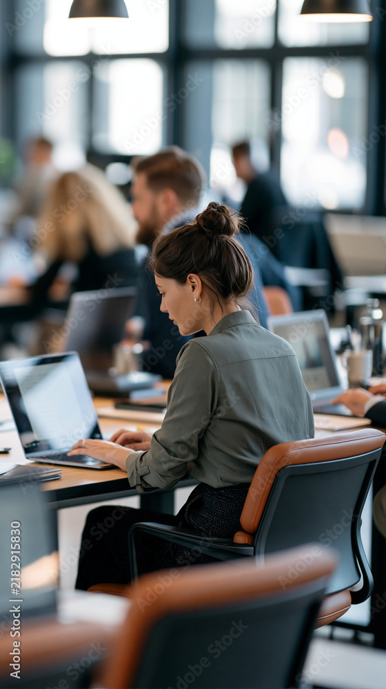 Fototapeta premium Rear view of a young couple sitting at desks with laptops preparing for an online meeting, bright open plan office background with large windows, remote meeting preparation,