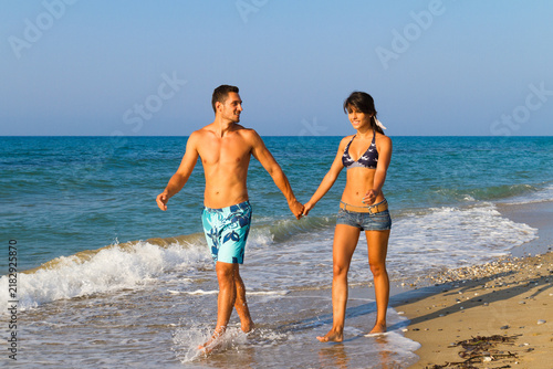 Happy cheerful young couple having fun playing tohether water splashing, laughing and jumping at the beach with the ocean in the background.