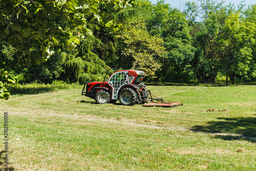Photography Tractor mows grass in a field surrounded by trees on a sunny day in a rural area
