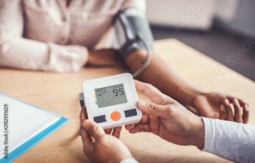 Foto Focused Male Patient Measuring Blood Pressure With Monitor In Clinic Setting, Sitting At Table With Caregiver Observing, Ensuring Accurate Health Check