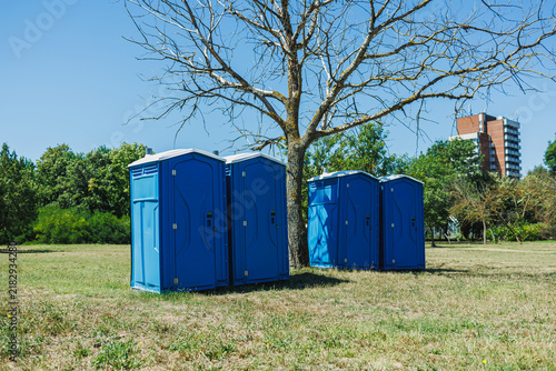 Canvastavla Portable toilets placed in a grassy area near a tree on a sunny day in a park se