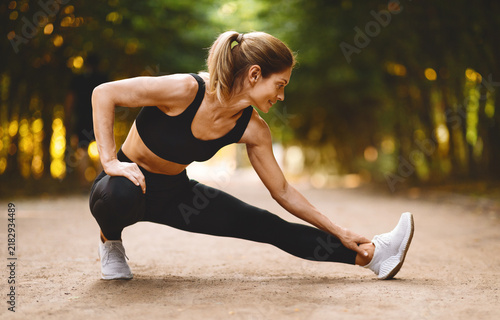 Картината върху платно Focused Fit Caucasian Woman Performing Leg Stretching Exercise Outdoors In Park, Embracing Healthy Lifestyle, Practicing Fitness In Nature, Enjoying Fresh Air And Sunshine